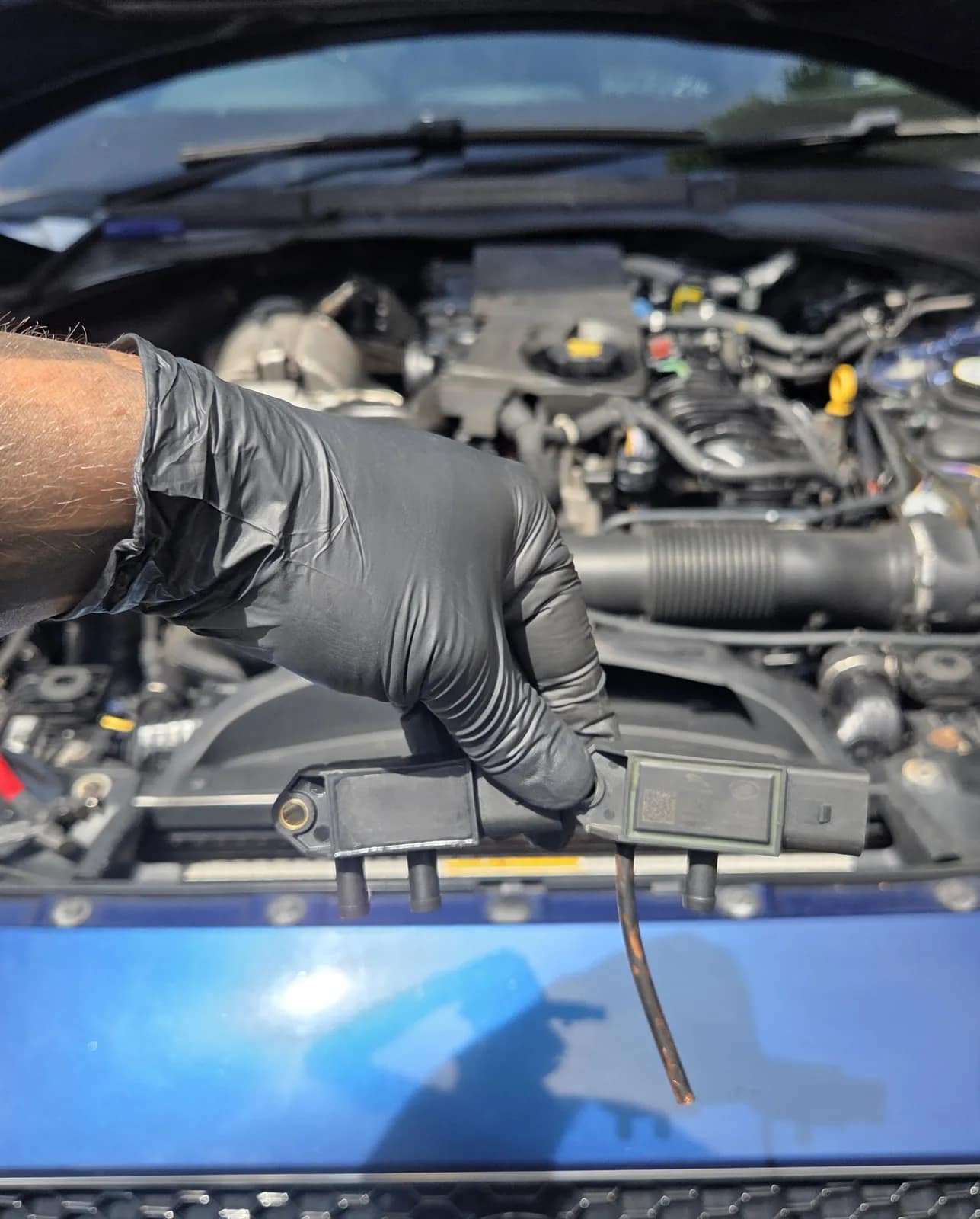 Gloved hand working on a sensor in a Jaguar XE engine bay