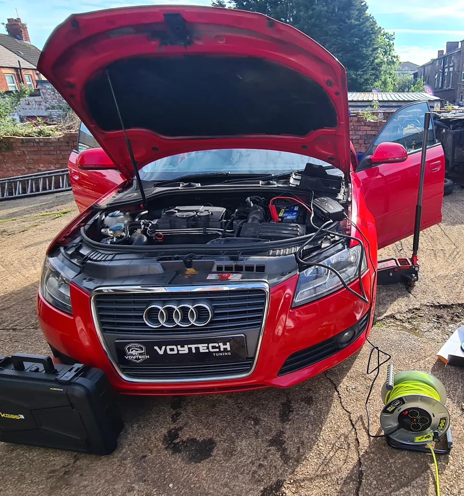 Red Audi A3 with the bonnet open and cables connected, tuning tool case in front