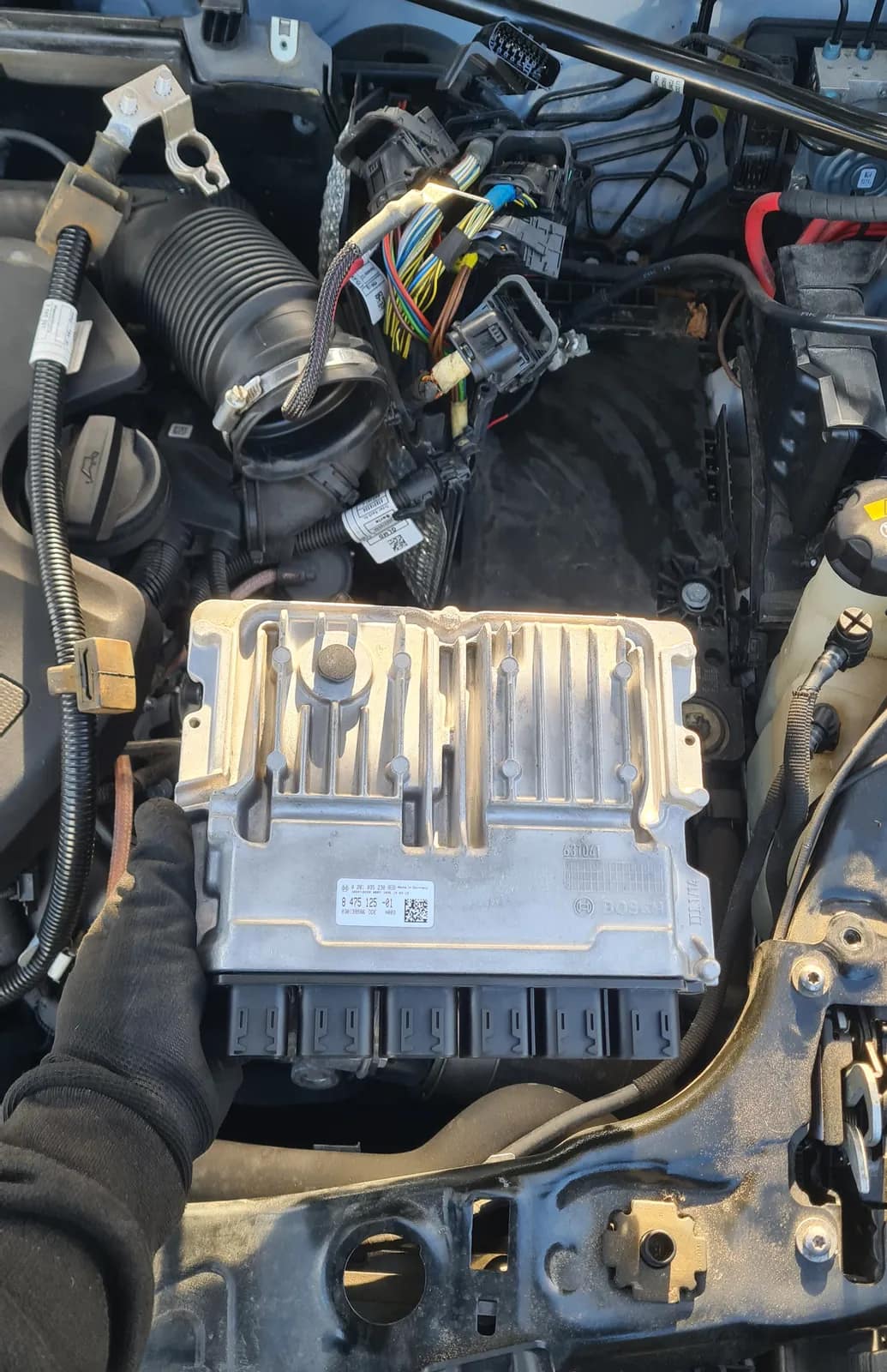 Engine control unit removed from a BMW and held over the engine bay