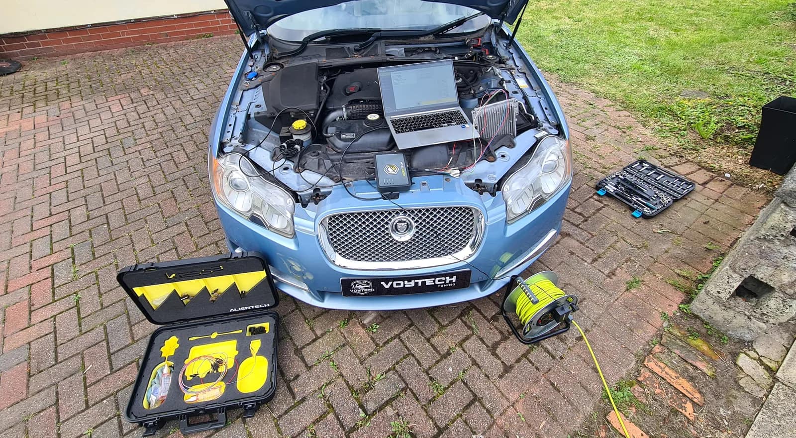 Ice blue Jaguar XF with a laptop and tuning tool connected under the bonnet, tool kit open on the drive
