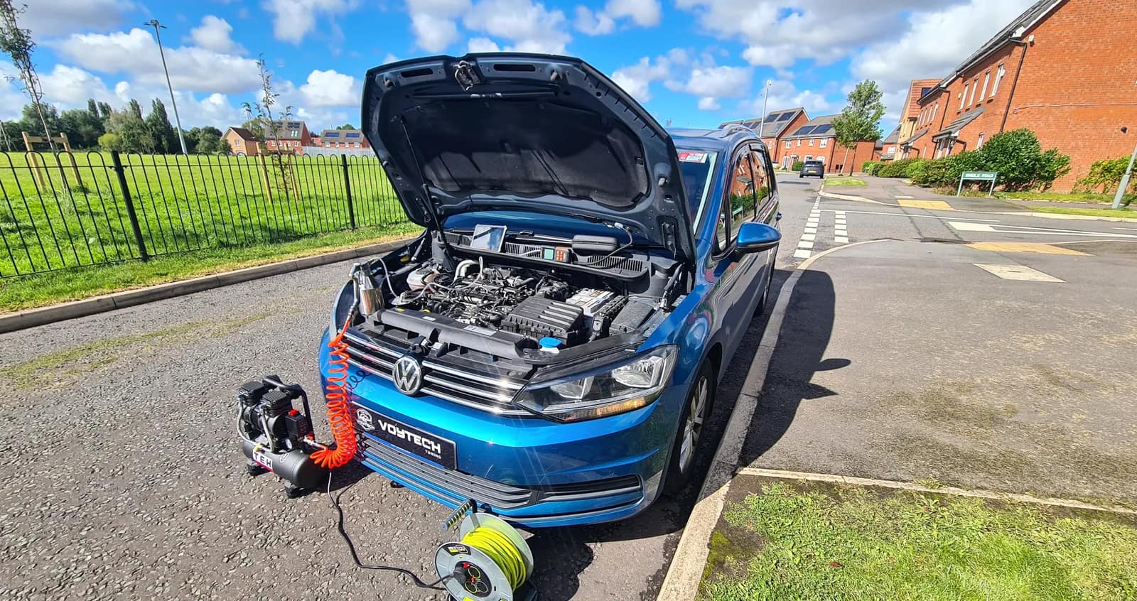 Blue VW Touran with the bonnet open and a DPF cleaning hose fed into the engine bay