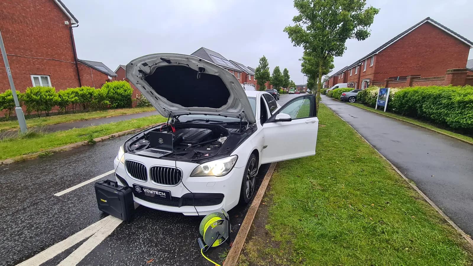 White BMW 7 Series on a street with the bonnet up and a laptop connected for diagnostics