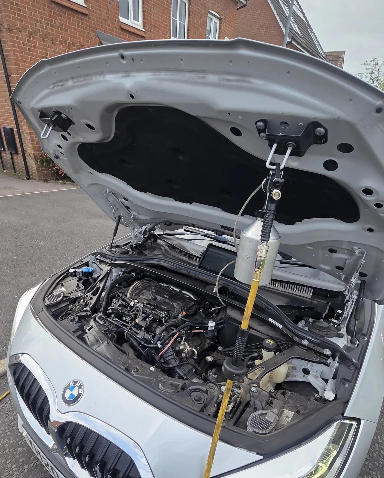 BMW 1 Series with the bonnet up and the DPF cleaning fluid bottle connected