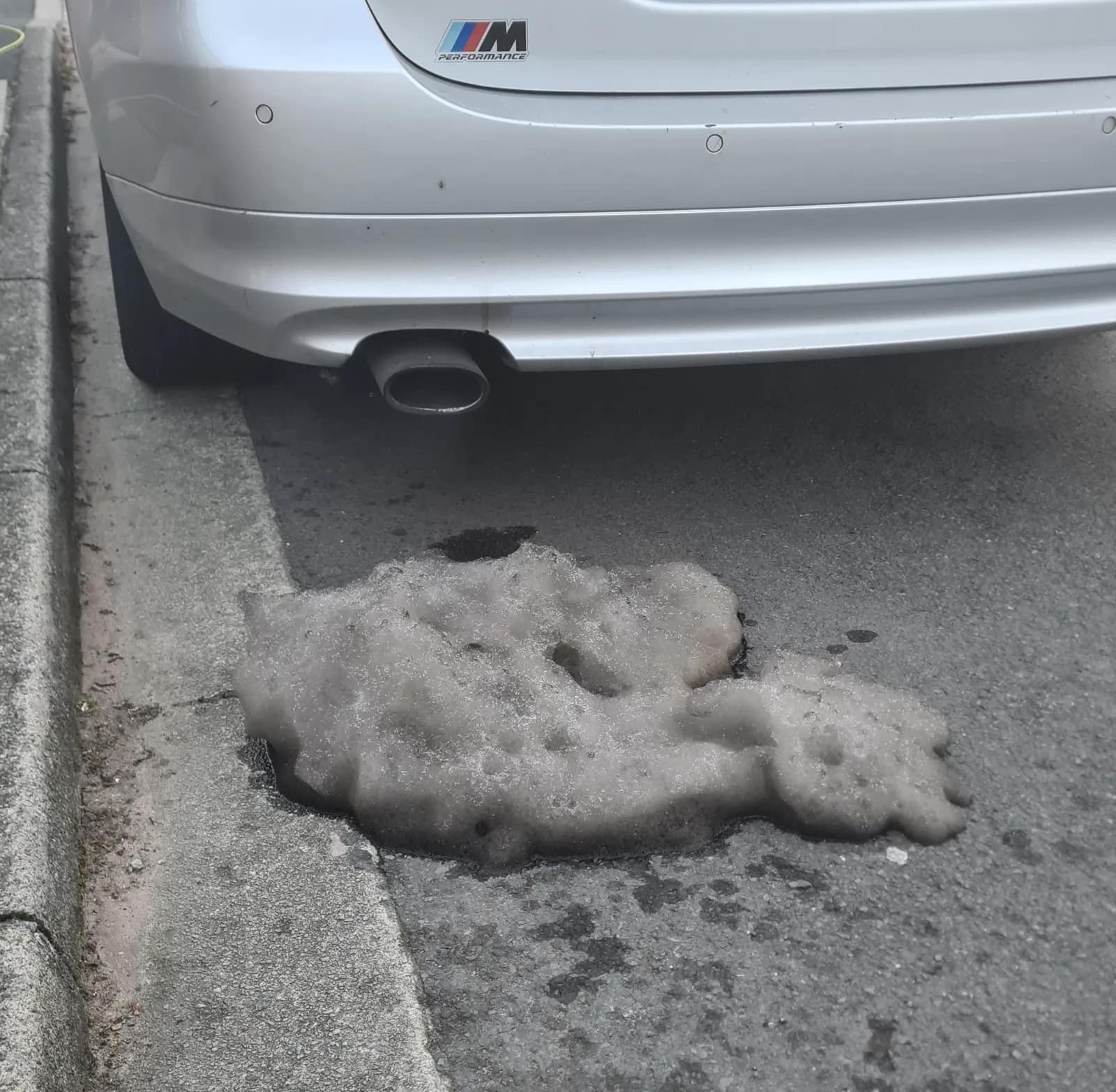 Soot and foam on the road below the exhaust of a silver BMW 3 Series after a DPF clean