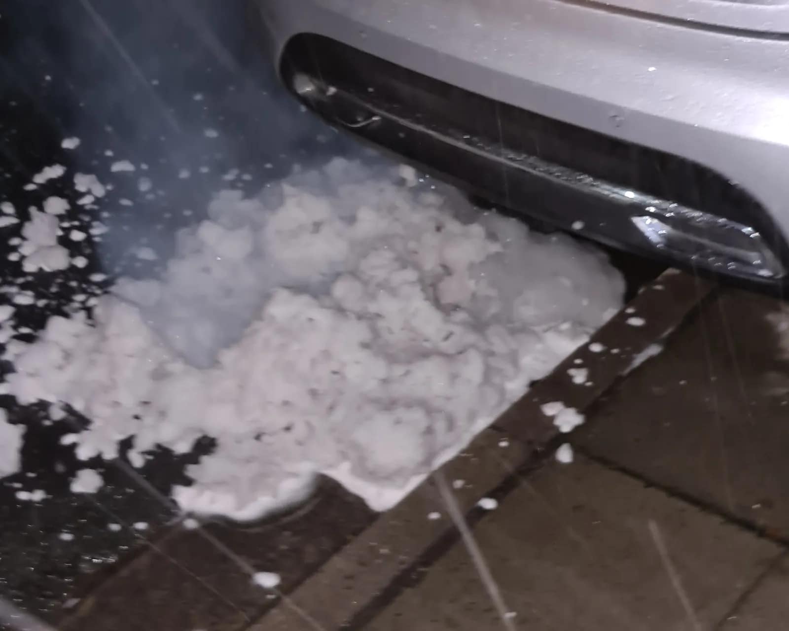 Pile of white DPF cleaning foam on the pavement under a car's rear bumper