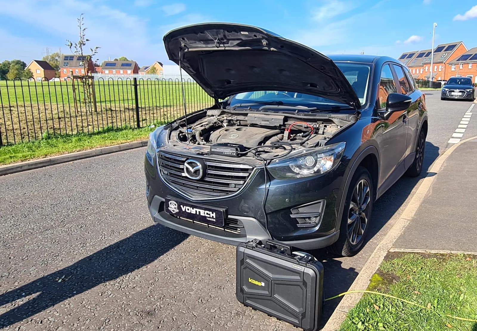 Grey Mazda CX-5 with the bonnet open and the tuning tool case on the road in front