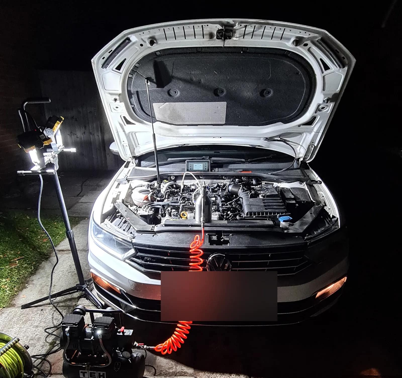 Silver VW Passat lit by a work light at night with a DPF cleaning hose running into the engine