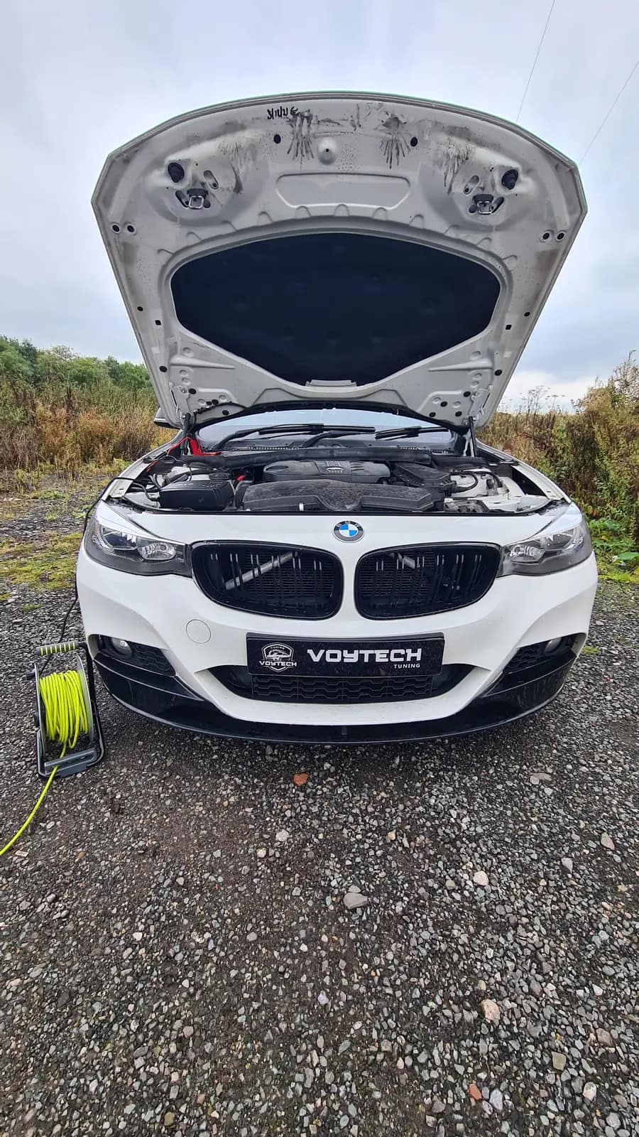 White BMW with a VOYTECH plate, bonnet up for a remap on a gravel drive