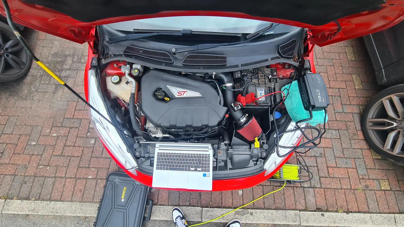 Laptop and tools beside the open engine bay of a red Ford Fiesta